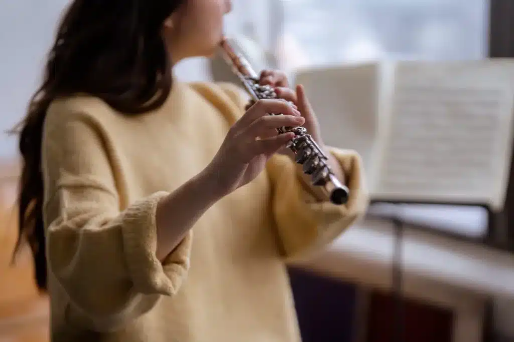 Mains tenant une flûte à bec au-dessus de partitions musicales en lumière naturelle