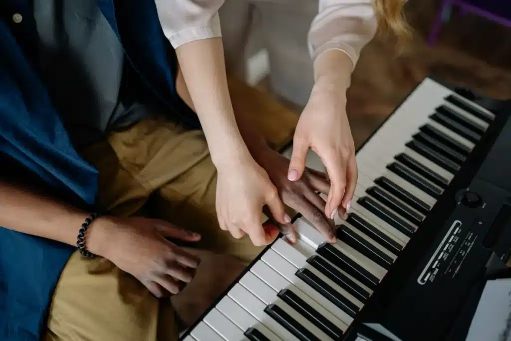 Mains d'enfant sur les touches d'un piano avec un guide adulte bienveillant à proximité