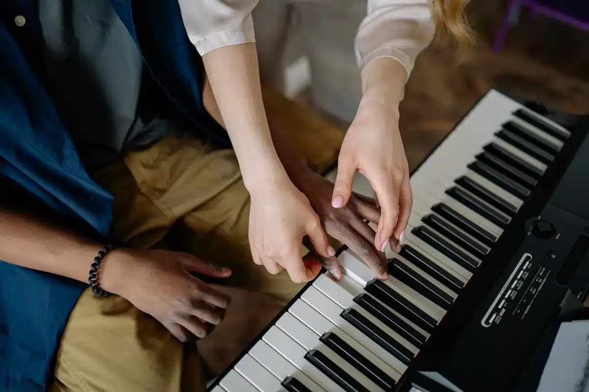 Mains d'enfant sur les touches d'un piano avec un guide adulte bienveillant à proximité